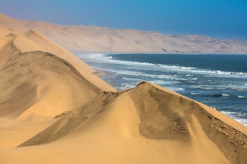 The concept of extreme and exotic tourism. Ocean surf with foamy waves. Gorgeous jeep - safari through the huge sand dunes. Atlantic coast of Walvis Bay, Namibia, south of Africa